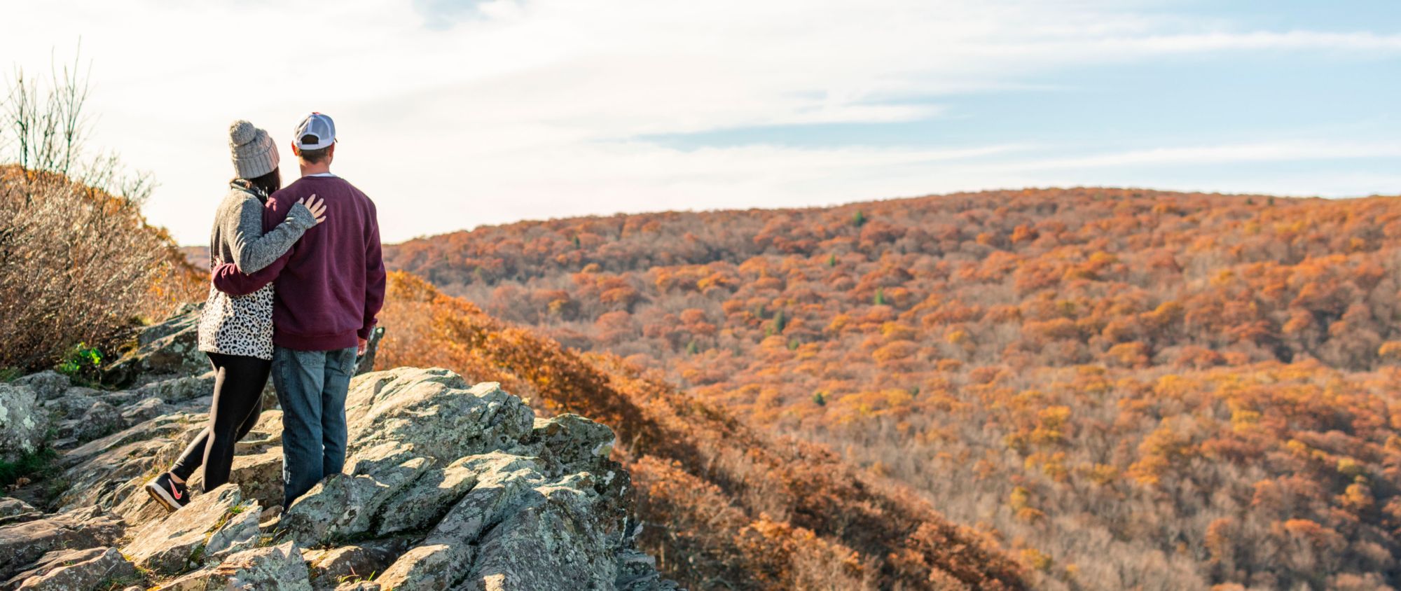 A couple overlooking autumn hills from a rocky trail.