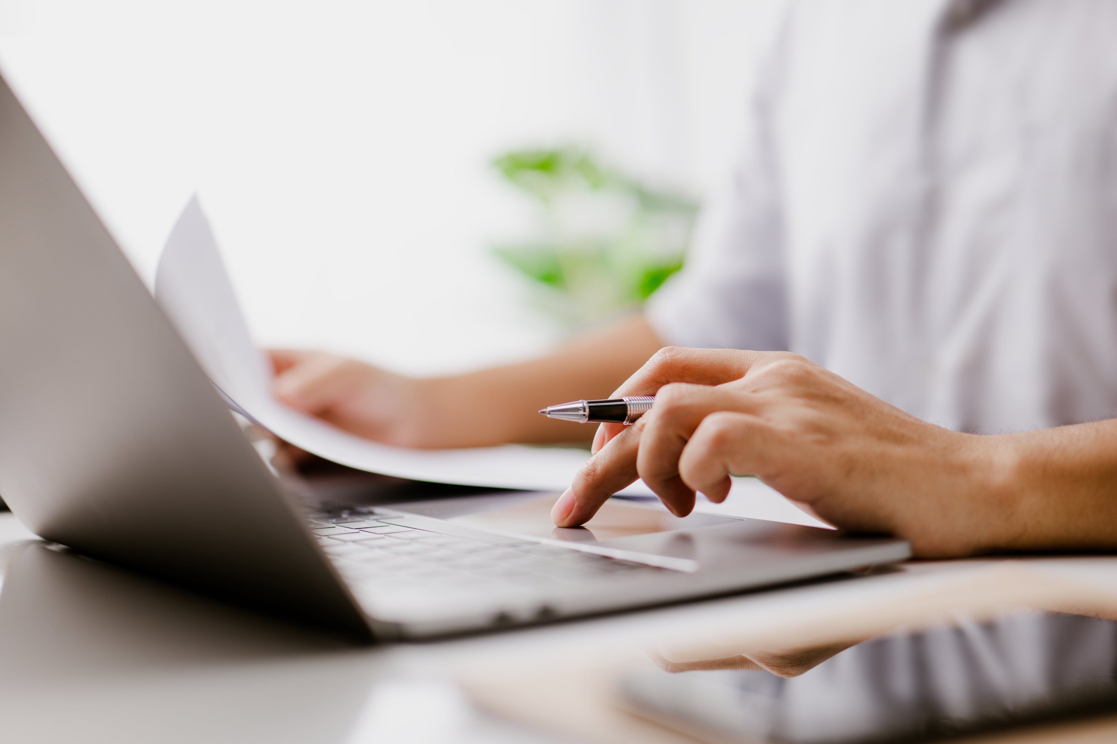 Person reviewing paperwork while using a laptop.