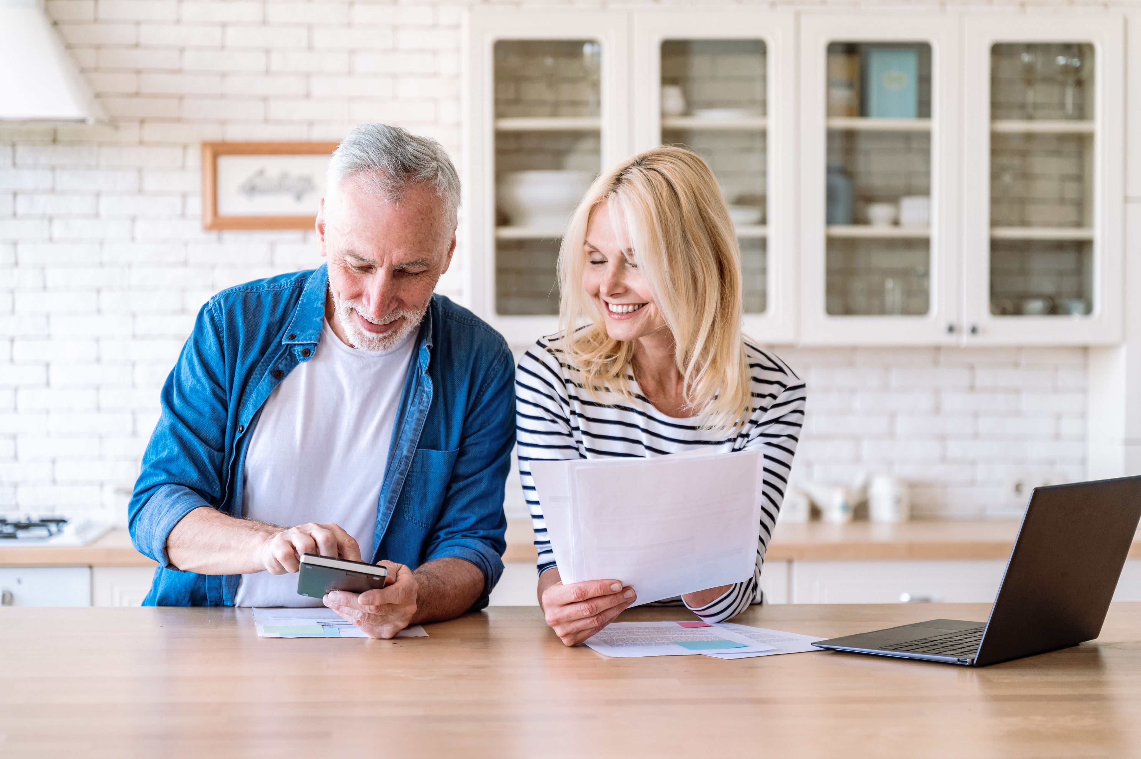 Retired couple reviewing financial paperwork together at their kitchen table.