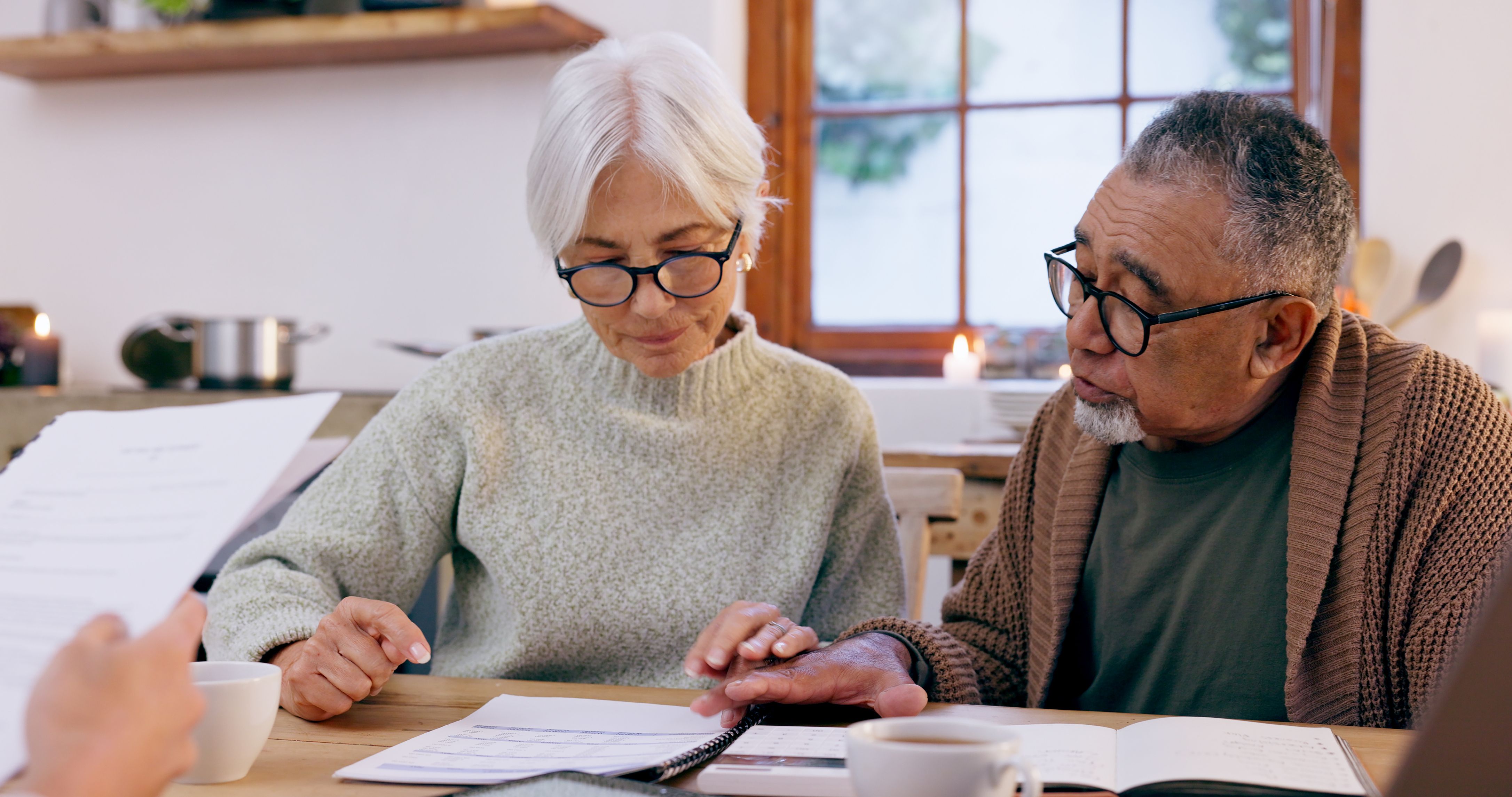 Older couple reviewing financial documents with an advisor at their kitchen table.