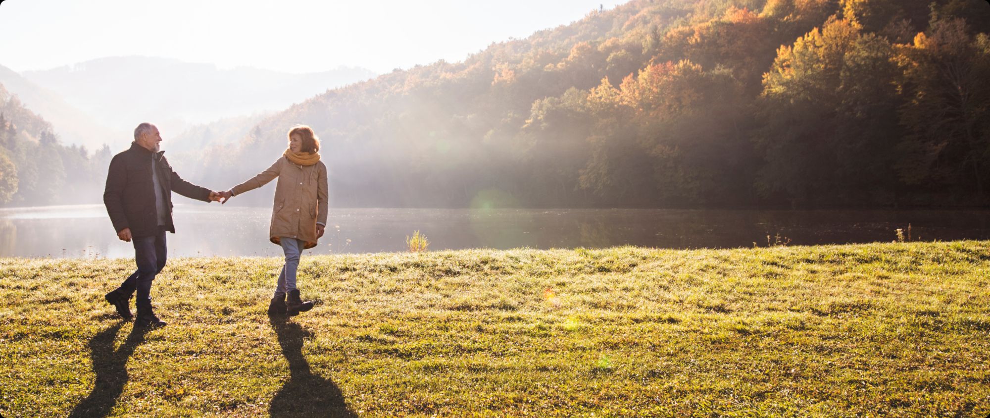 Couple holding hands beside a misty lake in autumn.