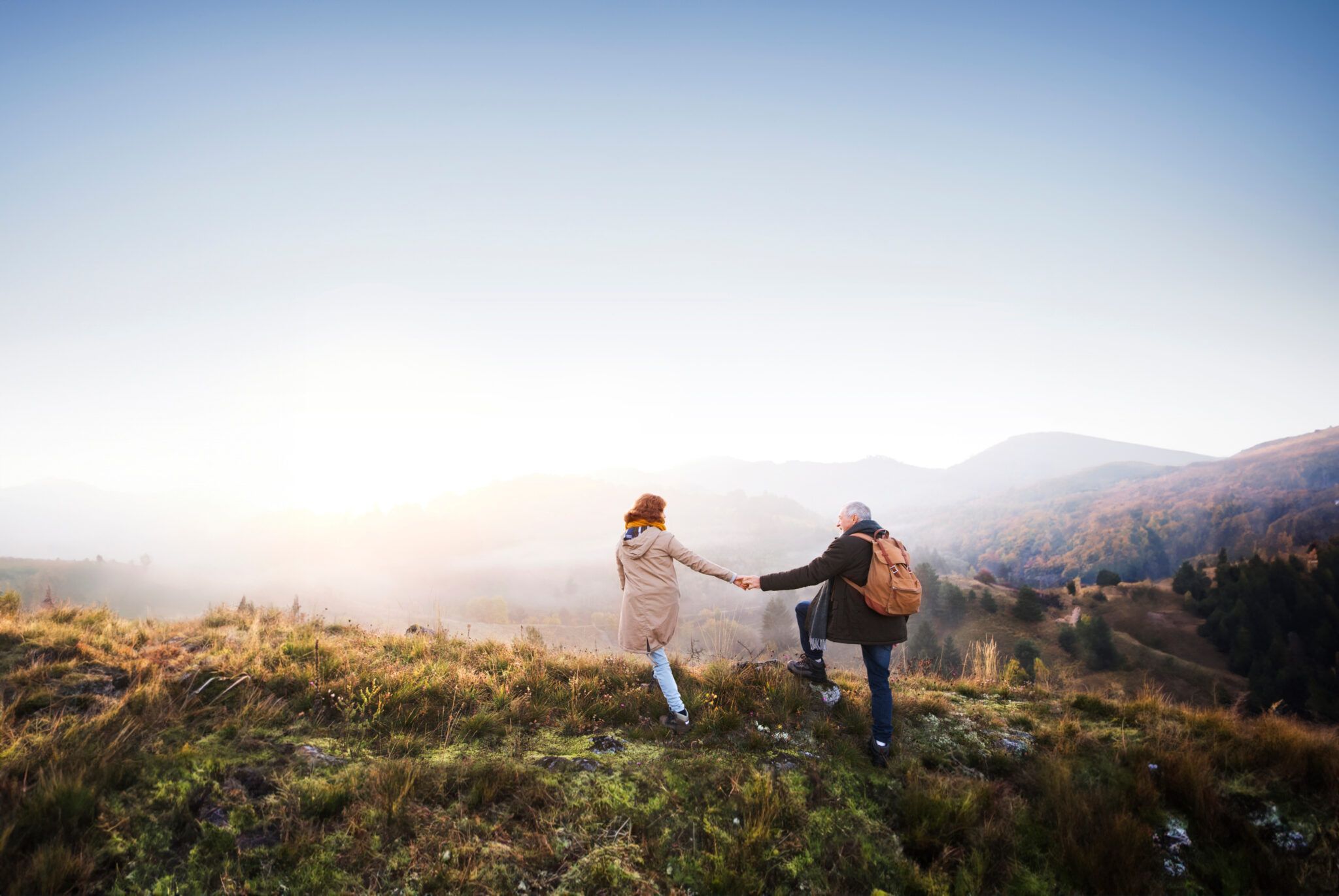Couple holding hands on a mountain trail at sunrise.